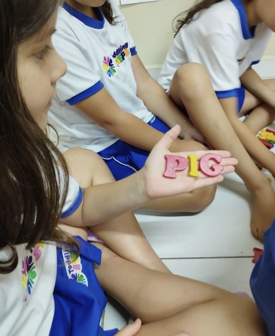 Criança segurando letras coloridas que formam a palavra PIG — aprendizado bilíngue concreto